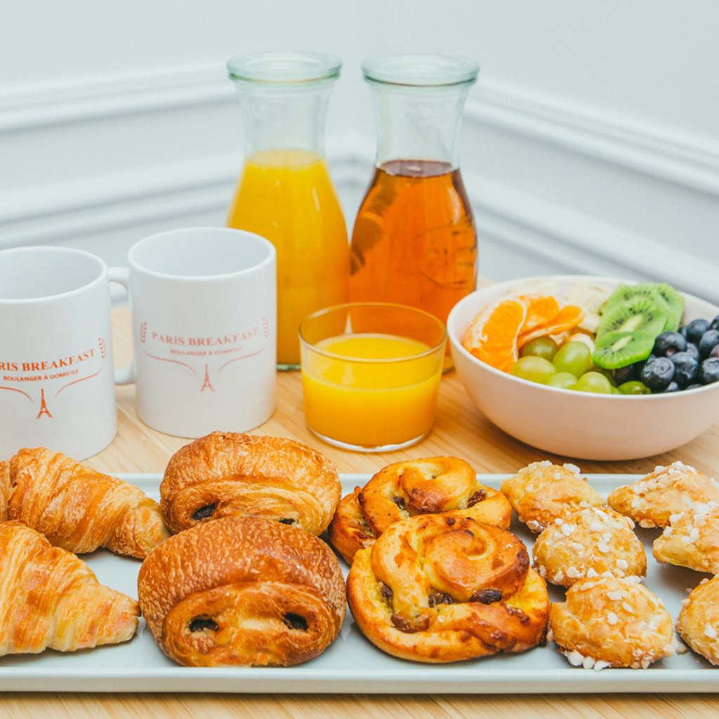 Viennoiseries fraîches, jus de fruits et bol de fruits variés, disposés pour une pause gourmande dans un cadre écologique.